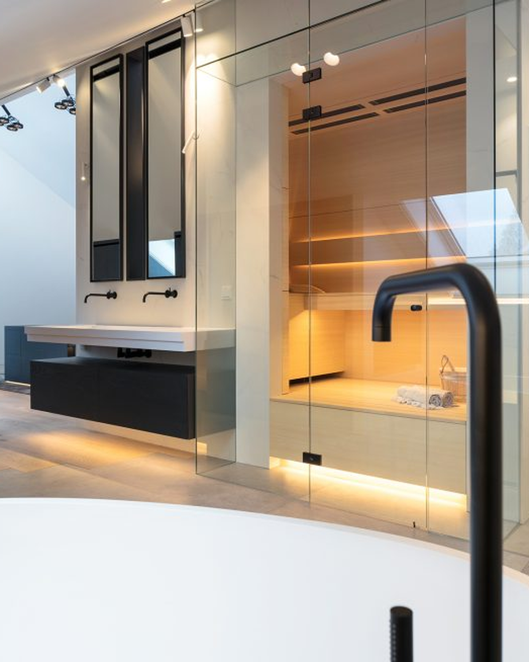 Modern bathroom with a glass-enclosed sauna, sleek black fixtures, large mirrors, and a minimalist white bathtub in the foreground.
