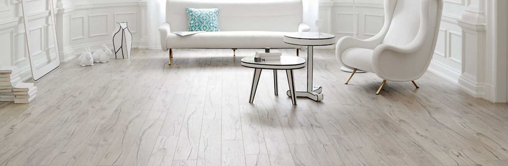 Minimalistische witte woonkamer met groot raam, moderne meubels, licht houten vloer en een witte fauteuil en sofa rond twee ronde salontafels.