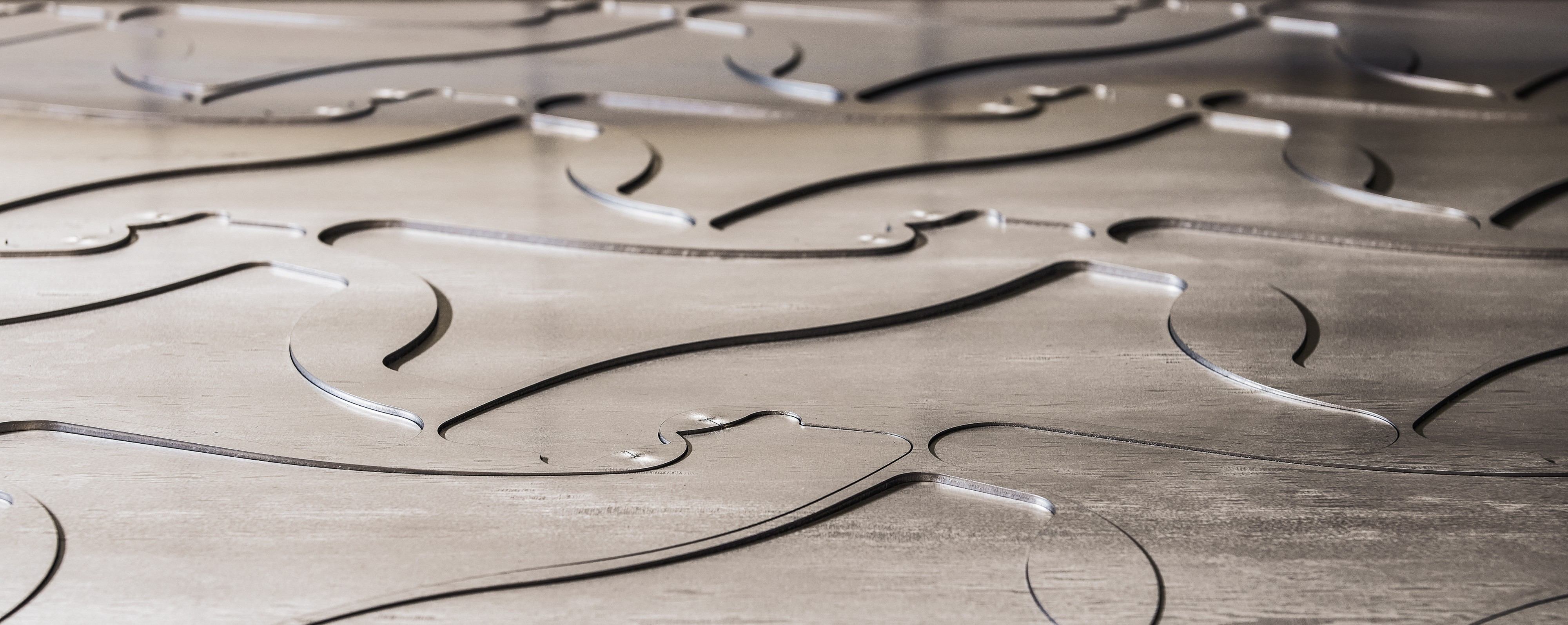 Nahaufnahme von geschichteten Metallplatten mit glatten, geschwungenen Ausschnitten, die fließende, wellenförmige Muster und schattierte Rillen bilden.