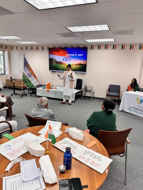 A person speaks to an audience in a room decorated with Indian flags for Republic Day. A screen displays "Republic Day" with a flag image.