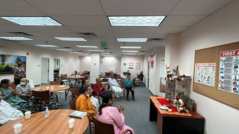 A group of people sitting in a room, engaged in a religious or cultural ceremony, with a decorated altar and posters on the wall.