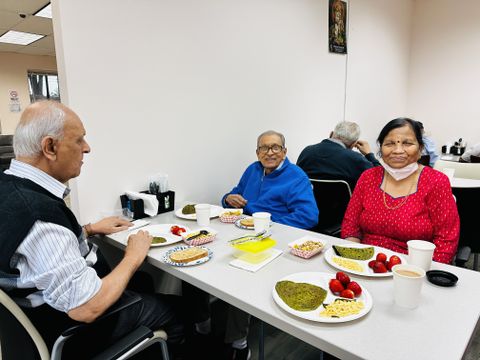 Three people sitting at a table with plates of food, including dhosas, fruit, and drinks, in a casual dining setting.
