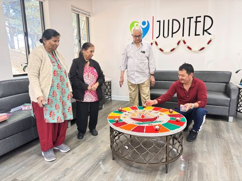 Participants gather around a table in a community room to perform a puja ritual.