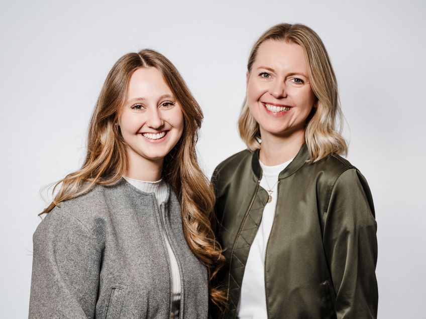 Zwei Mitarbeiterinnen aus dem Team Talent Acquisition stehen nebeneinander und lächeln in die Kamera.