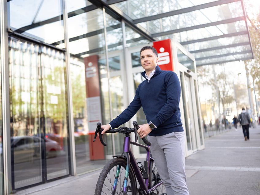 Mitarbeiter steht mit einem Fahrrad vor dem modernen Bürogebäude.