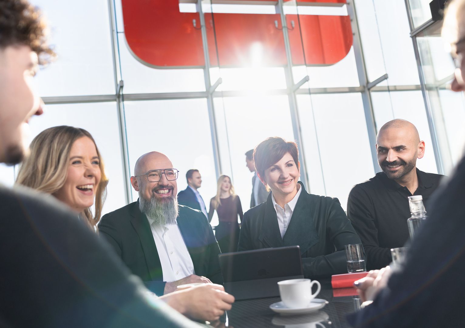 Mehrere Mitarbeitende sitzen gemeinsam an einem Tisch, tauschen sich aus und lachen gemeinsam