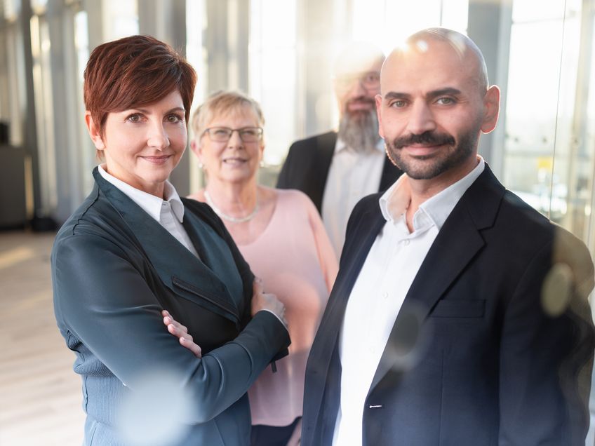 Vier Mitarbeitende stehen gemeinsam und hintereinander in einer Gruppe in einem modernen Arbeitsumfeld.