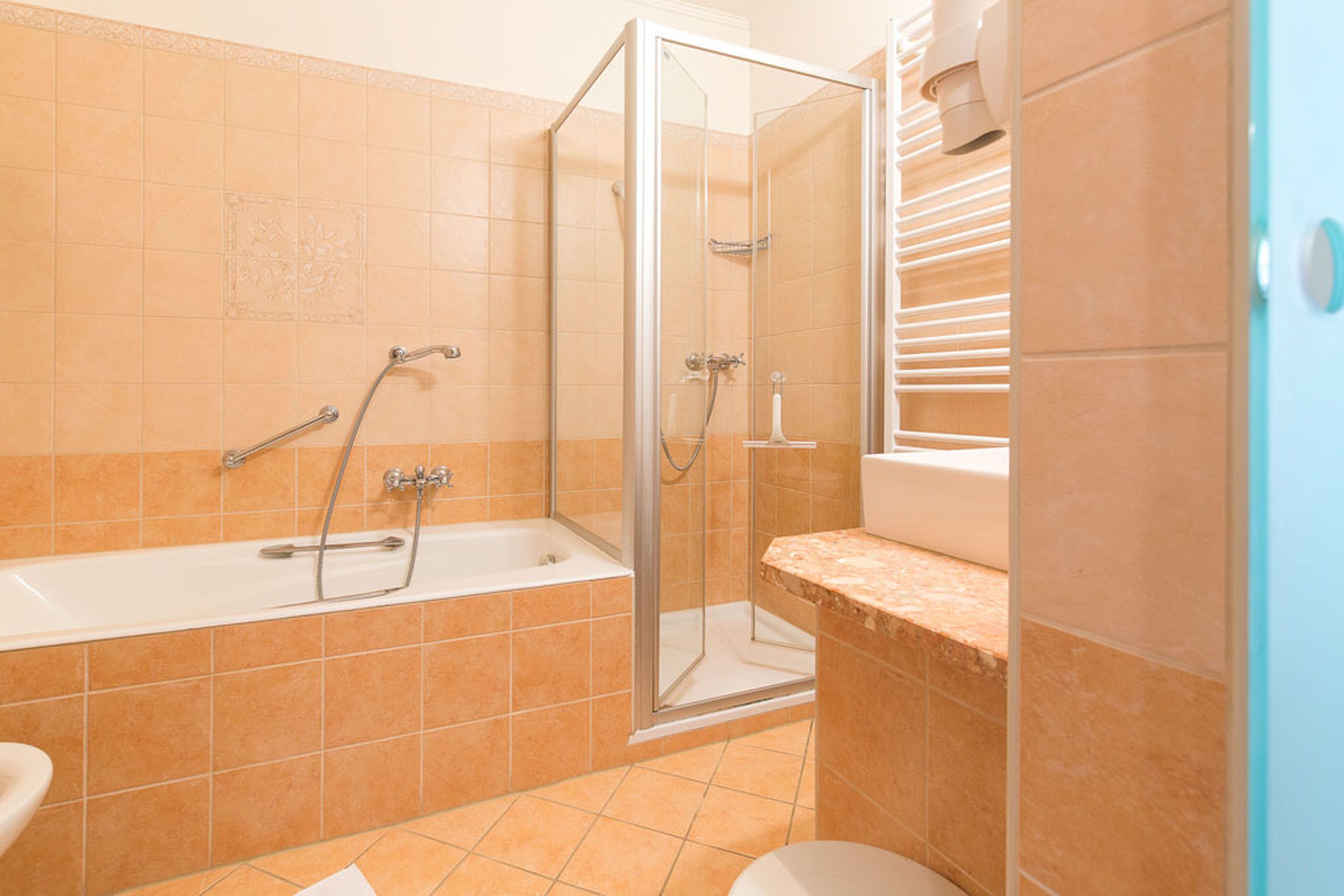 Ein Badezimmer mit beigefarbenen Fliesen, einer Badewanne mit Duschkopf, einer Dusche mit Glaskabine, einem Waschbecken mit Marmorplatte und einem Handtuchheizkörper.