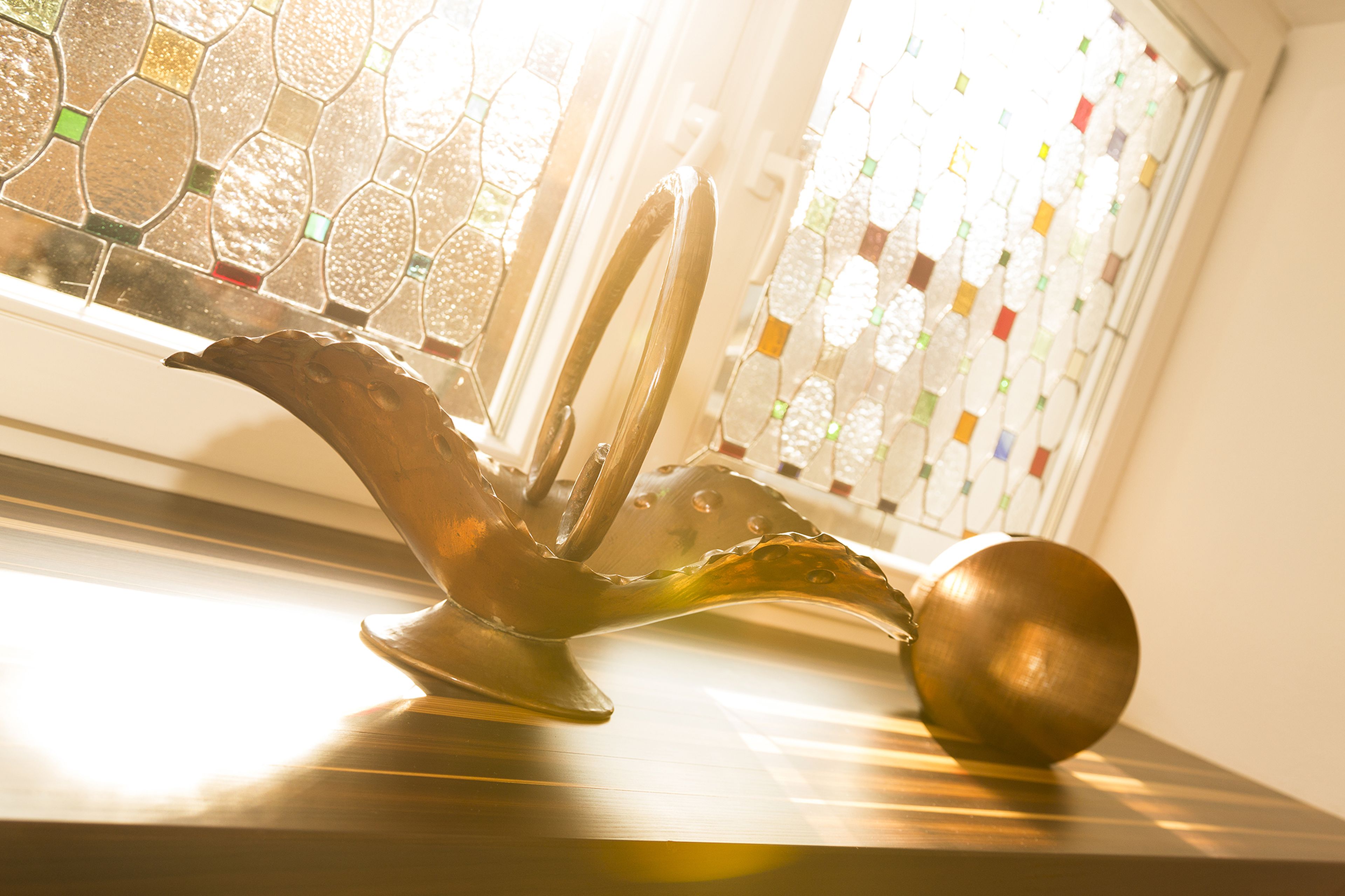 A bronze decorative sculpture and a spherical ornament on a sunlit windowsill with stained glass, casting warm light and shadows.
