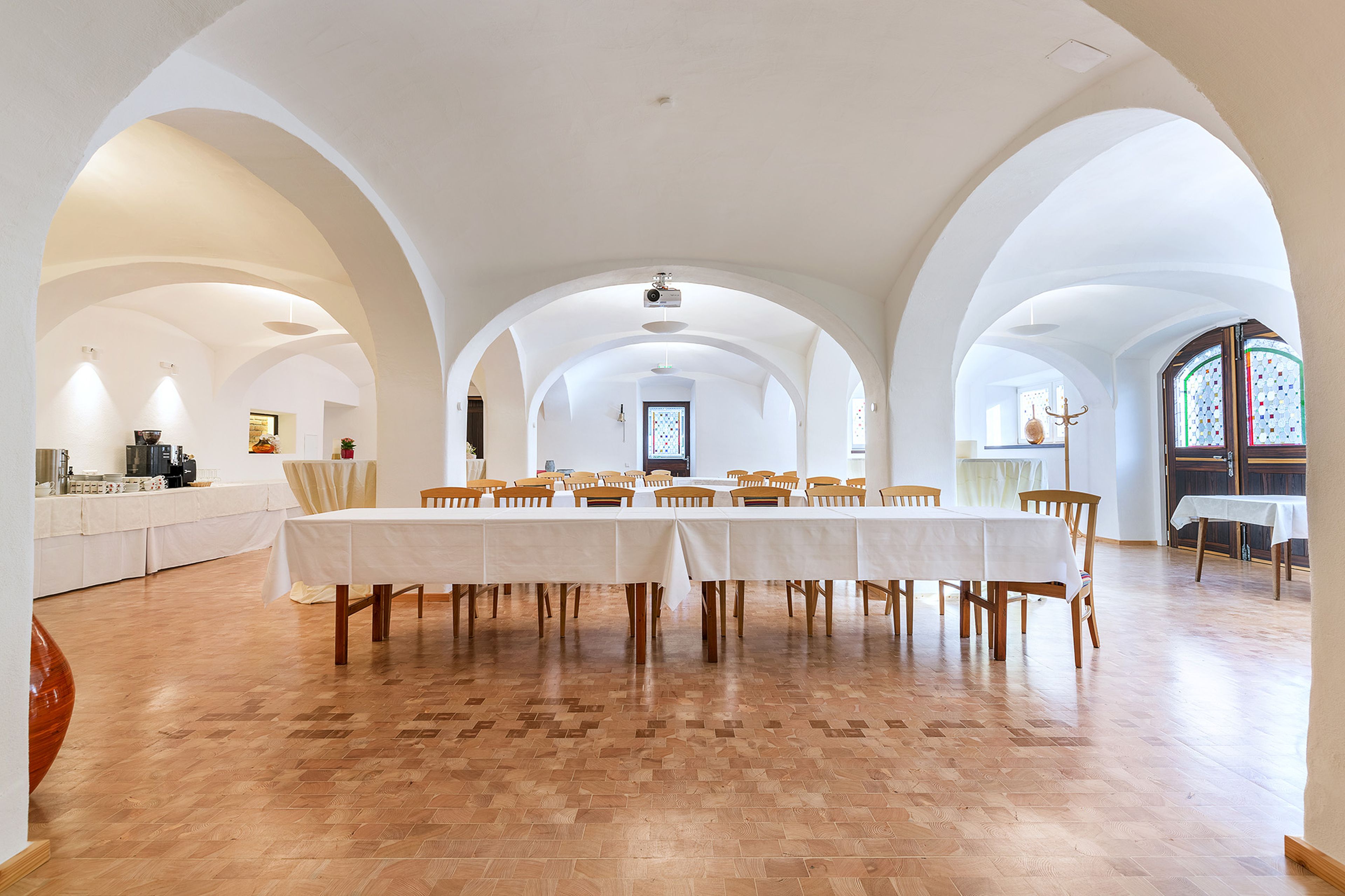 Geräumiger Bankettsaal mit gewölbten Decken, runden und rechteckigen Tischen, weißen Tischdecken und einem Buffetbereich mit gestapelten Tellern.