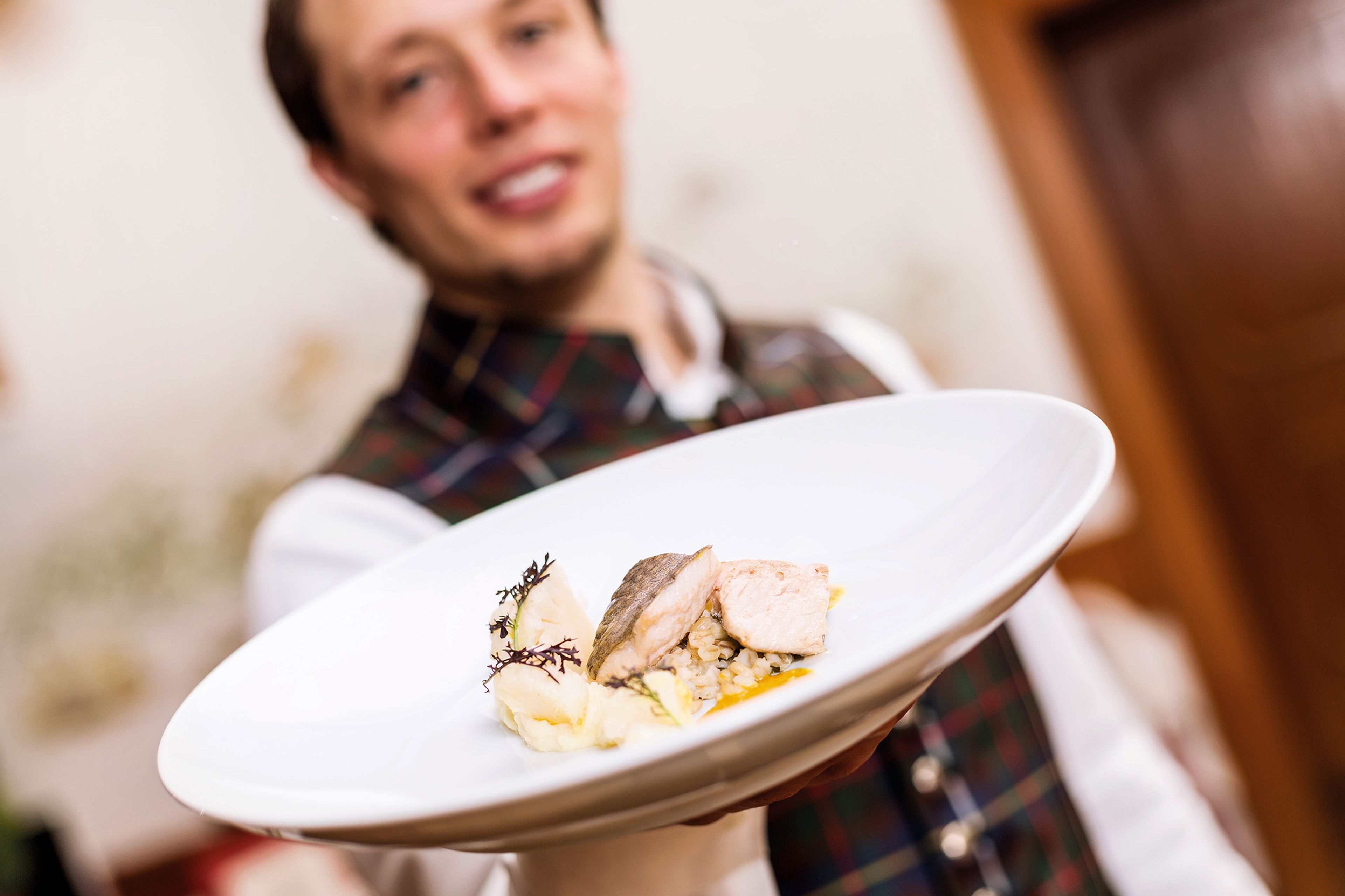 Johann Steinwender präsentiert ein Gourmetgericht mit Fisch auf einem weißen Teller.