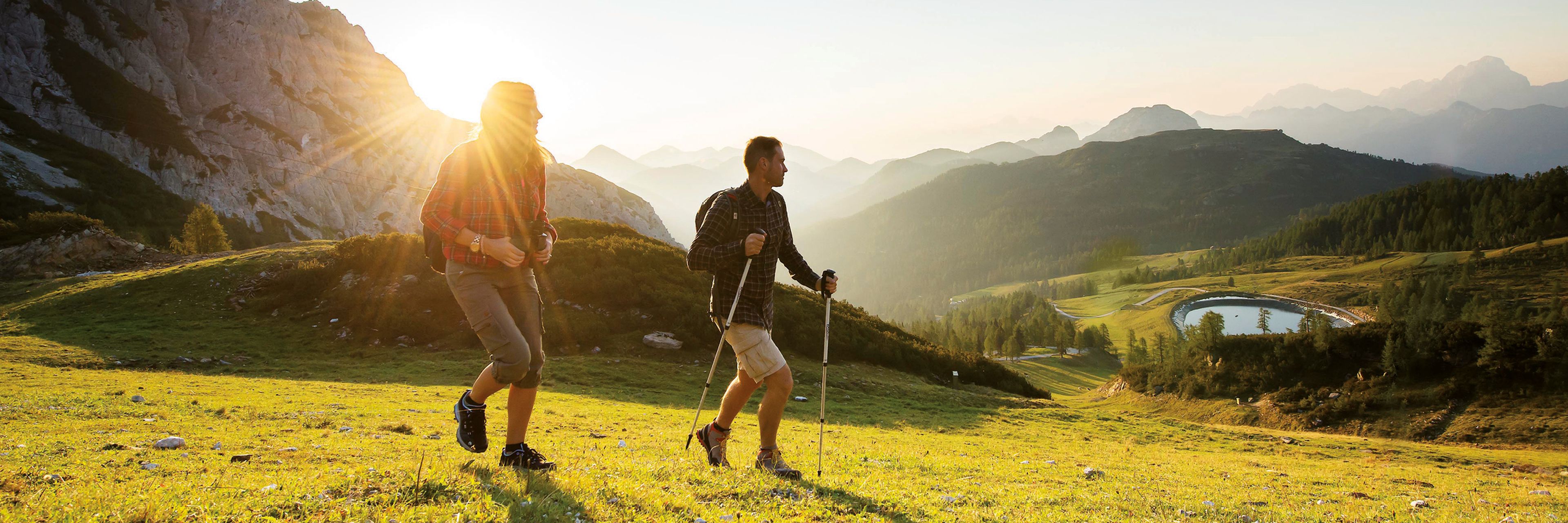 Zwei Wanderer im Nassfeld-Gebiet. Im Hintergrund der Sonnenaufgang und ein wunderschönes Bergbanorama.