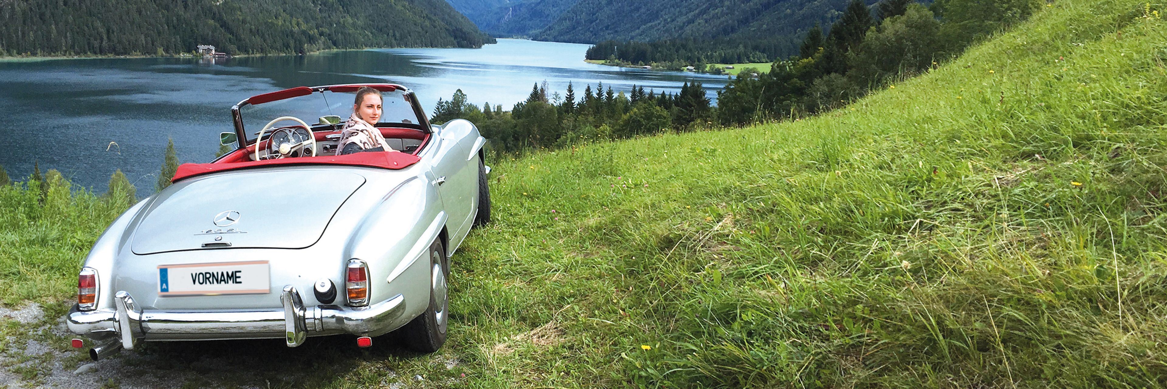 Slibernes Cabrio, das auf der Wise vor einem Blauen See steht
