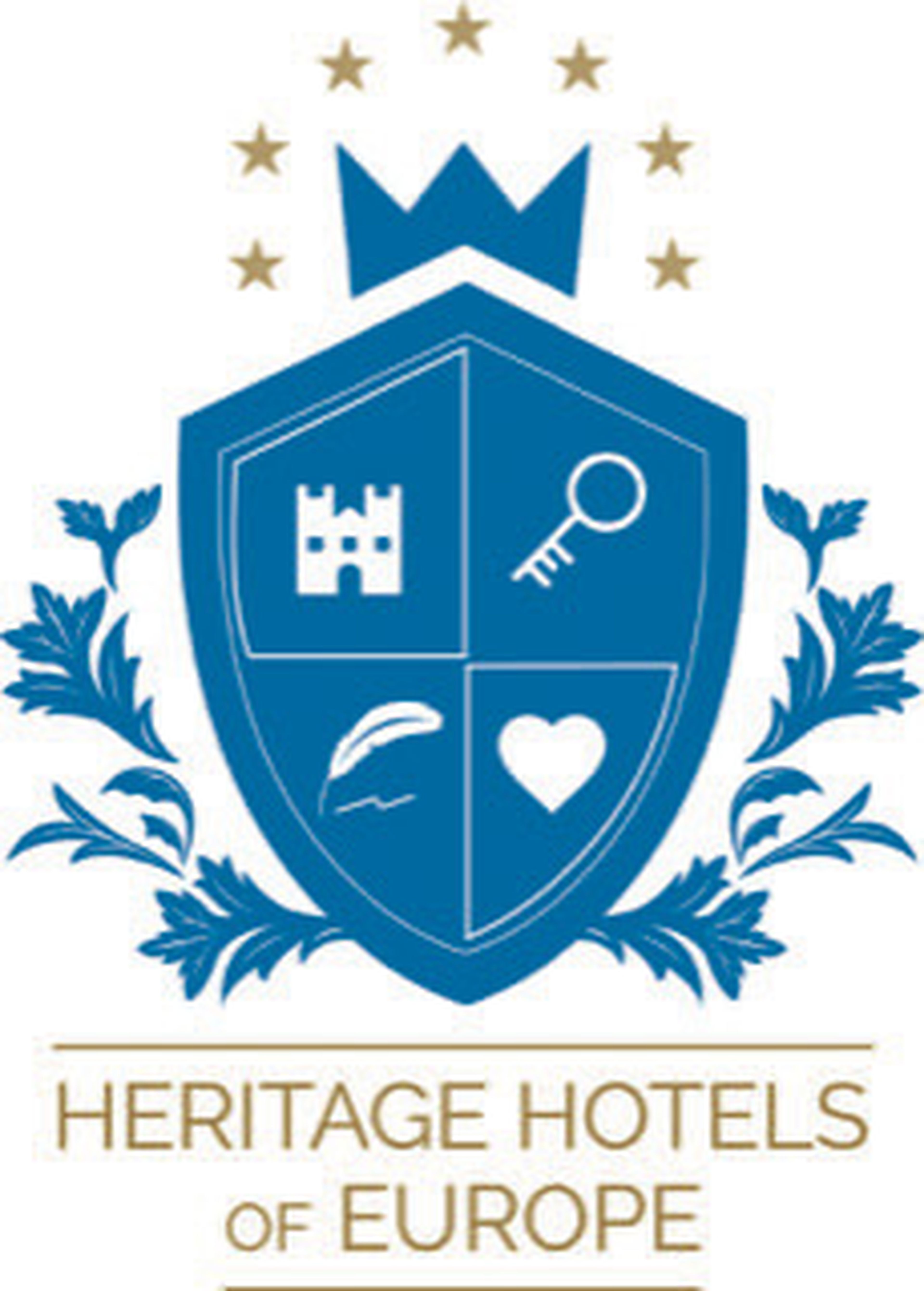 Blaues Schild mit einem Schloss, einem Schlüssel, einer Feder und einem Herz, gekrönt von einer Krone und Sternen. Der Text darunter lautet „Heritage Hotels of Europe“. Florale Akzente an den Seiten.