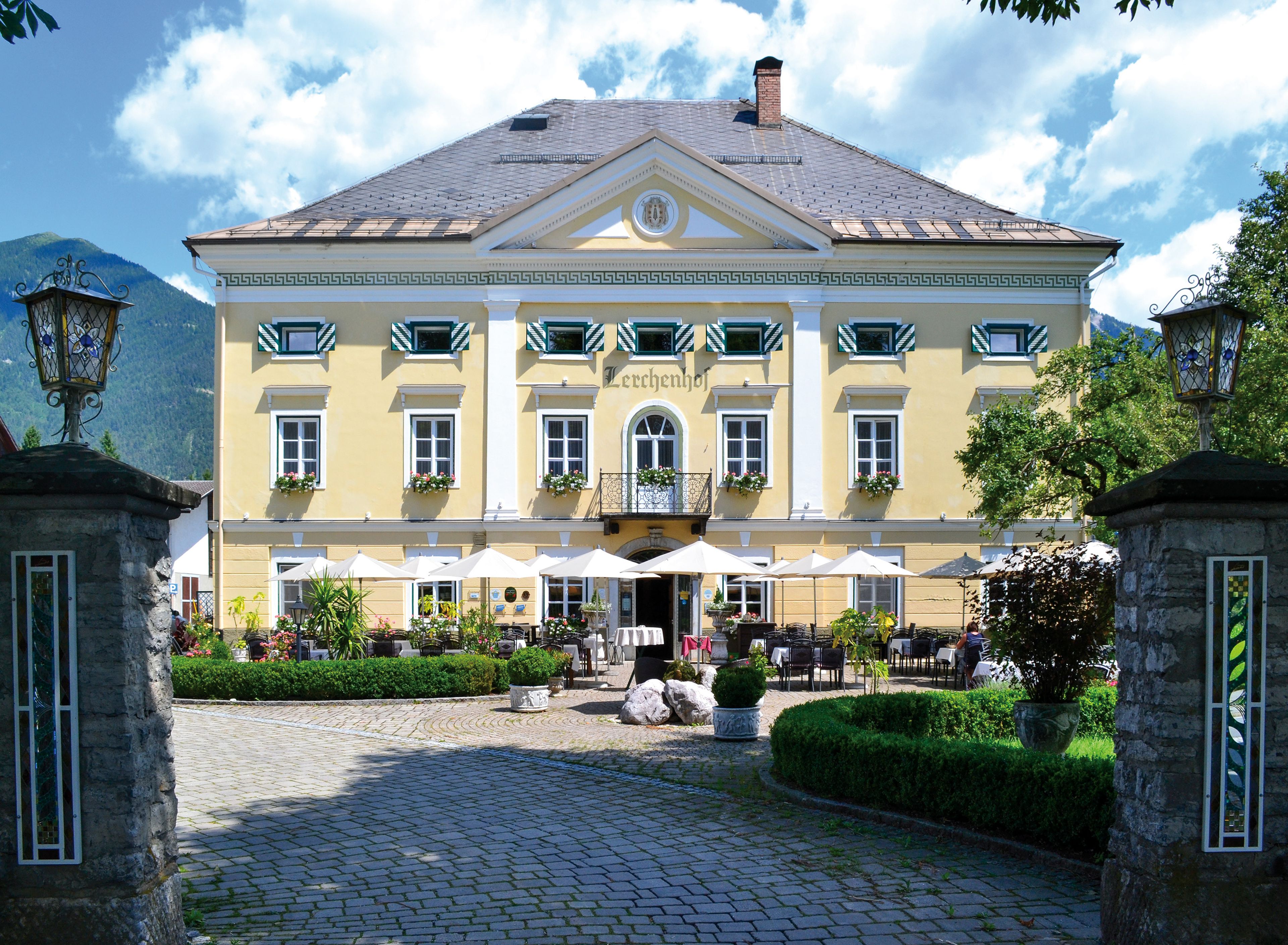 Ansicht Schloss Lerchenhof im Sommer mit Terrasse und Garten. Im Vordergrund das Einfahrts-Tor