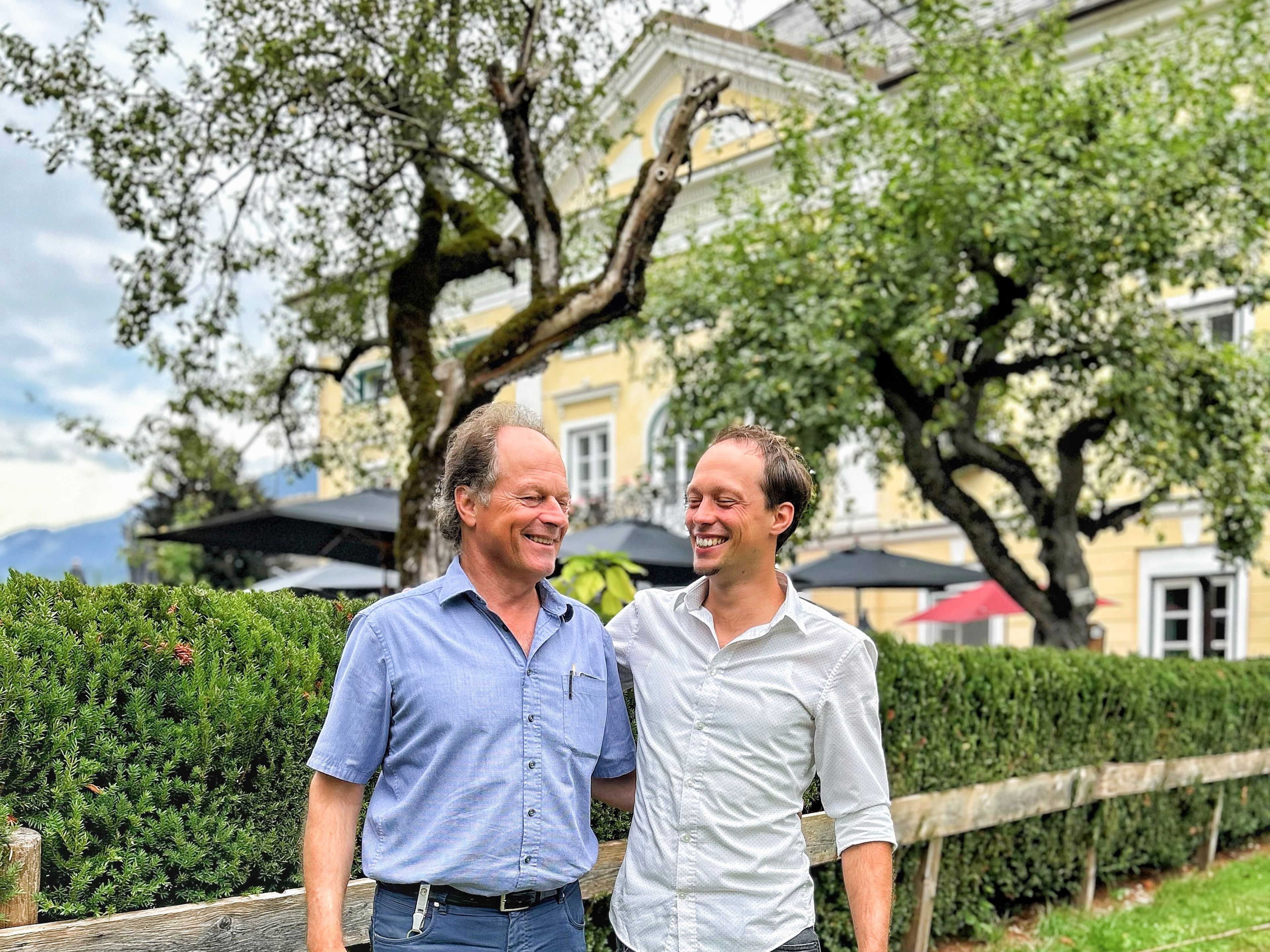 Hans und Johann Steinwender lachen herzlich. Im Hintergrund das Schloss Lerchenhof