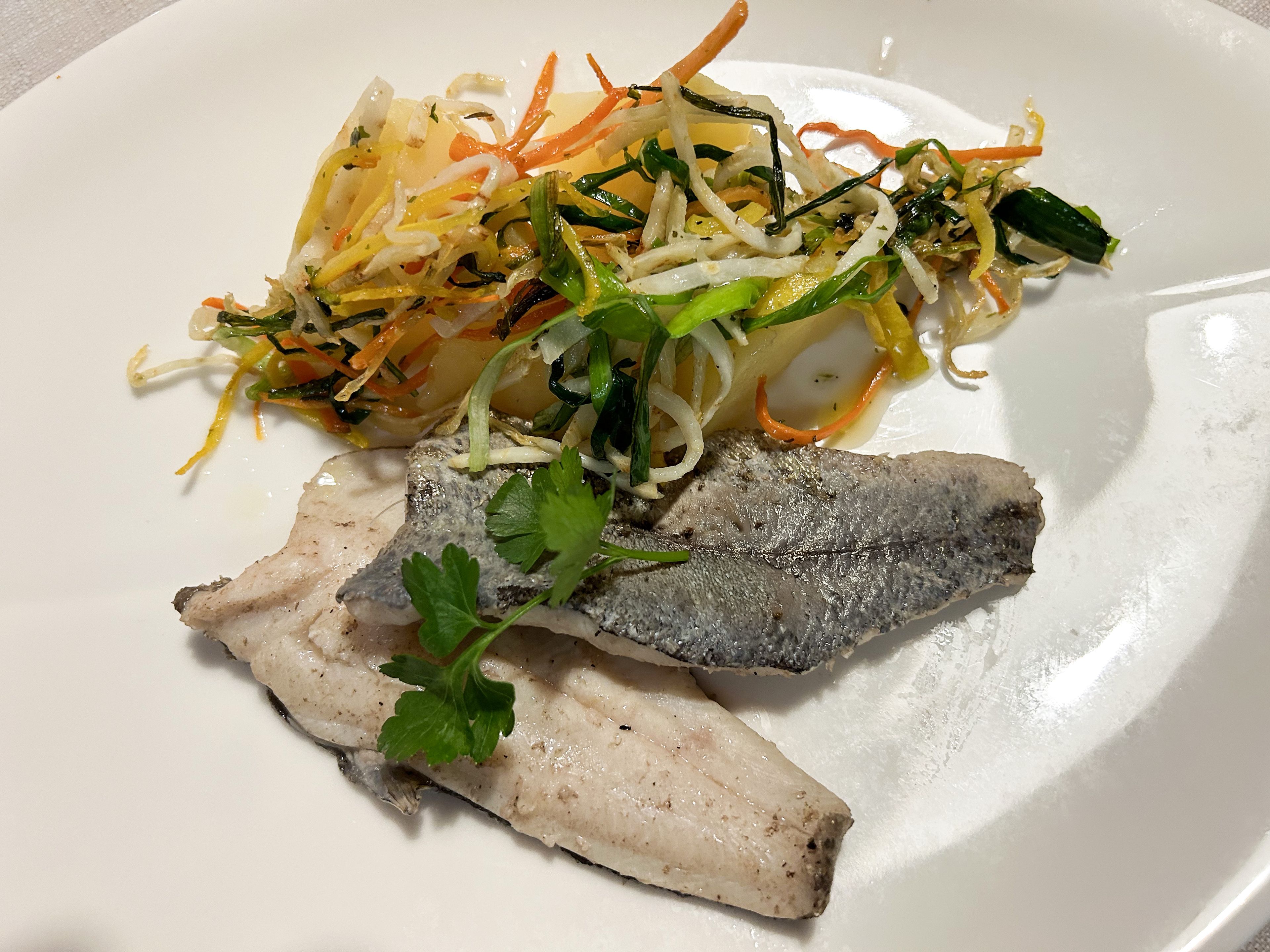 Gegrillte Fischfilets, garniert mit Petersilie, serviert mit einer Beilage aus buntem sautiertem Gemüse auf einem weißen Teller.