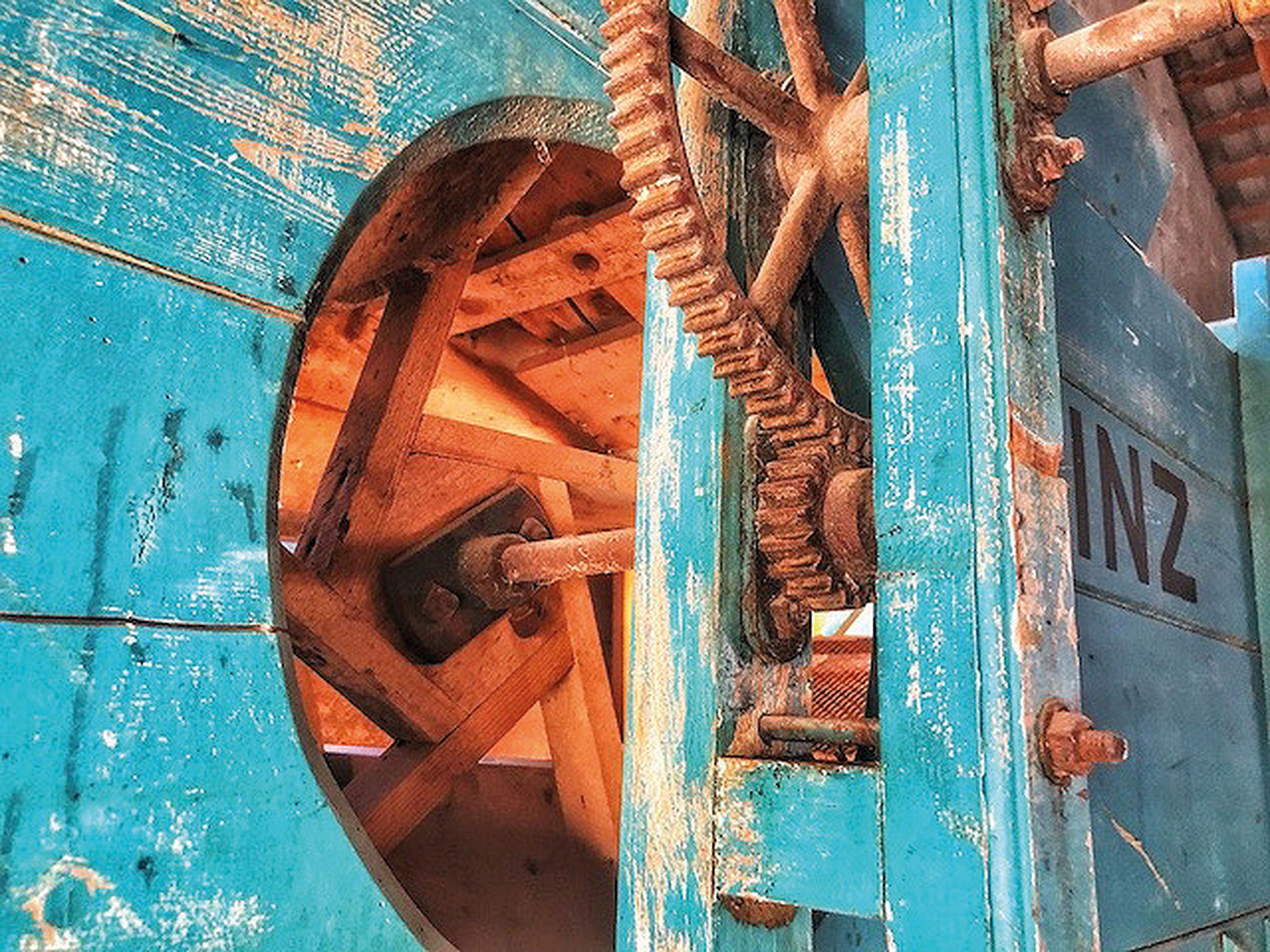 Nahaufnahme einer alten blauen Holzmaschine mit sichtbaren Zahnrädern und einer runden Öffnung, die den Blick auf die hölzernen Innenkomponenten freigibt.