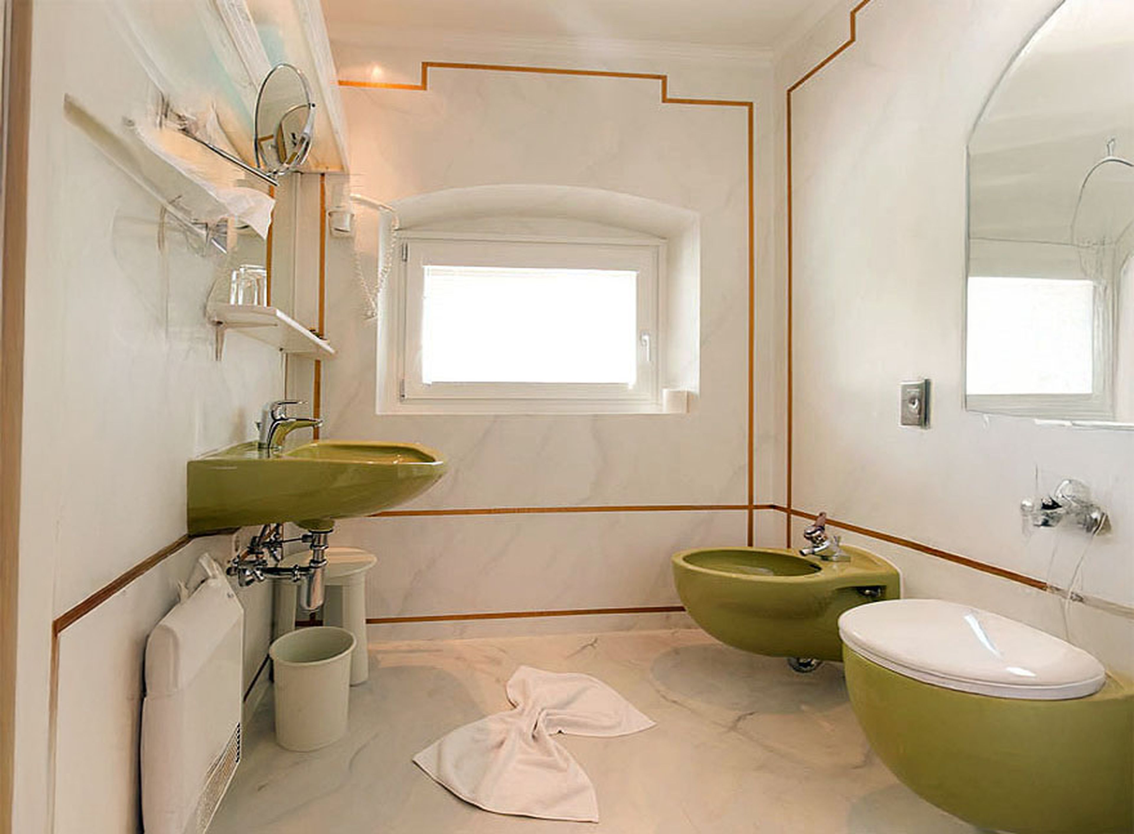 Bathroom with white marble walls, green sink, bidet, and toilet. Large mirror, small window, and a towel on the floor. Modern and clean design.