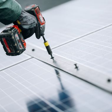 Nahaufnahme wie eine Person mit einem Akkuschrauber Solarpaneele befestigt.
