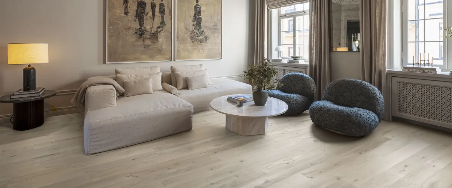 Elegant living room with light wood flooring, neutral-toned furniture, and large windows.