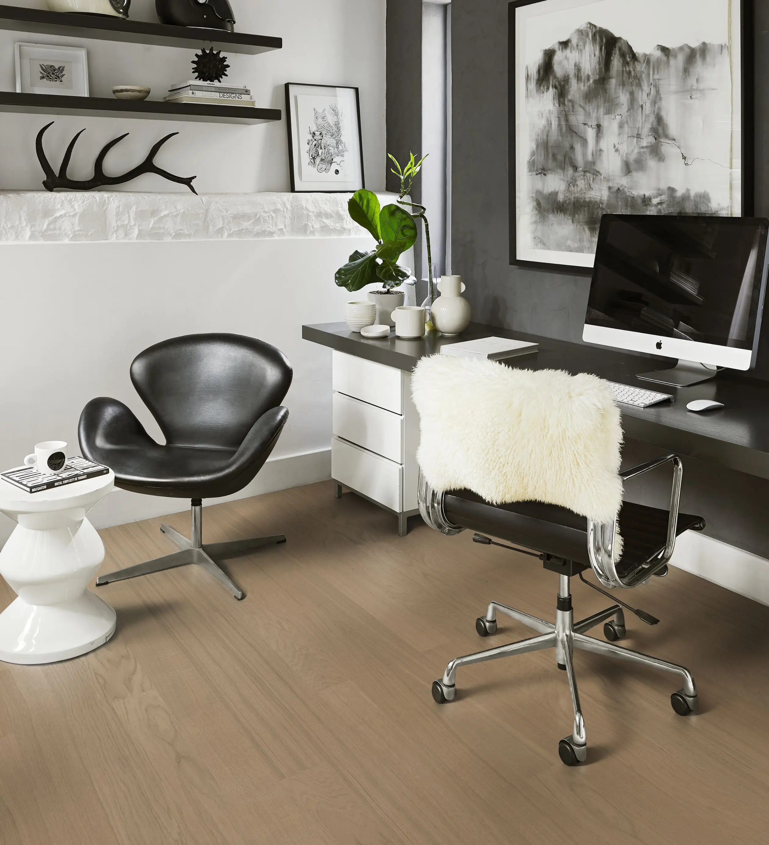 A sleek and minimalist office featuring light wooden floors, a black leather chair, and a white desk with a faux fur cushion, enhanced by monochrome decor.