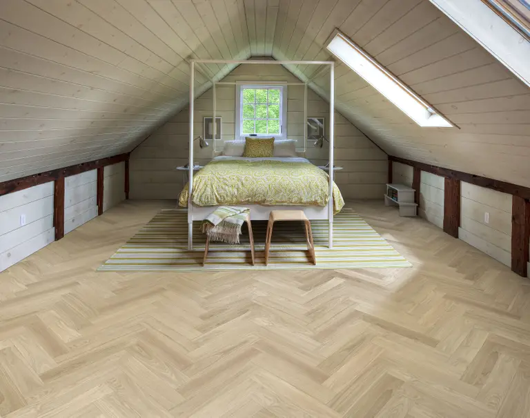 Attic bedroom with a sloped ceiling, featuring a bed with yellow bedding, a striped rug, and wooden floors. Natural light from skylights.