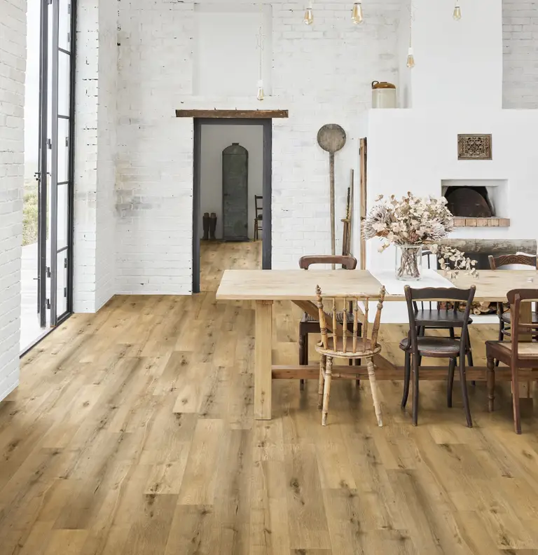 Spacious dining area with wooden table, mixed chairs, and hardwood floor. White brick walls, fireplace, and large windows enhance the rustic charm.