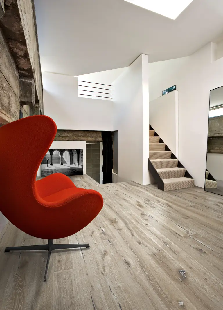 Oak Aspeland. A contemporary loft with light, textured oak flooring, a bold red lounge chair, and a floating staircase.