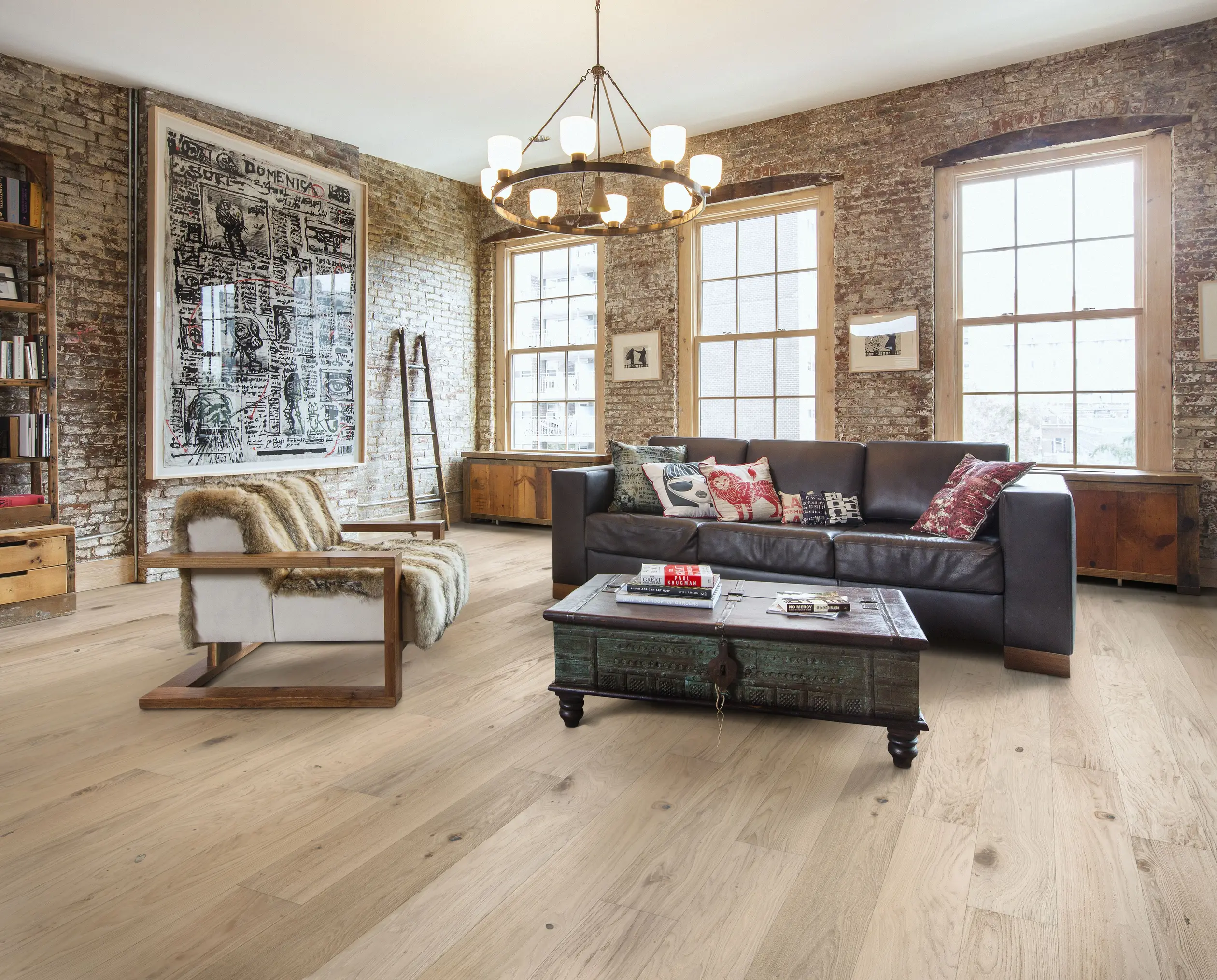 Cozy living room with a brown leather sofa, rustic armchair, wooden coffee table, and exposed brick walls, lit by a chandelier.