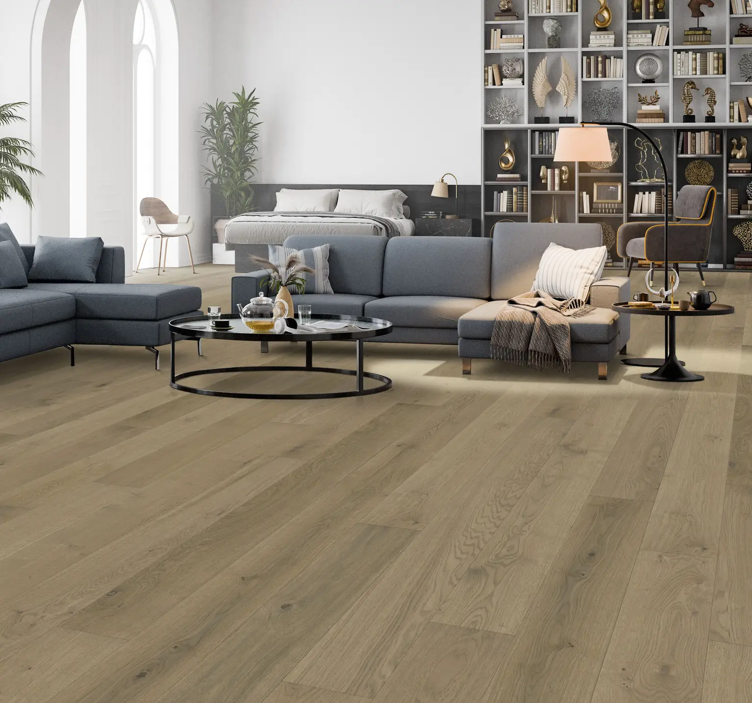 Modern living room with a gray sectional sofa, round coffee table, and shelves filled with decor. Large windows and wooden floor enhance the space.