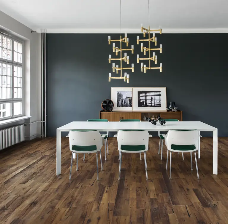 Modern dining room with a white table, six chairs, dark accent wall, wooden floor, large window, and geometric pendant lights.