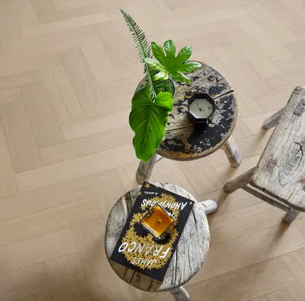 Three rustic wooden stools with plants, candles, and a book on a herringbone-patterned wooden floor.