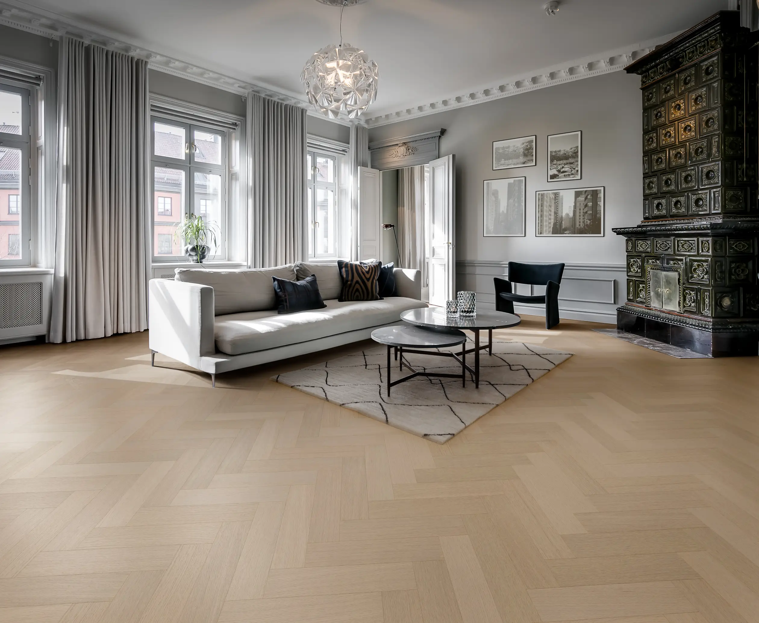Spacious living room with a white sofa, round coffee table, patterned rug, large windows, and a decorative tiled stove.