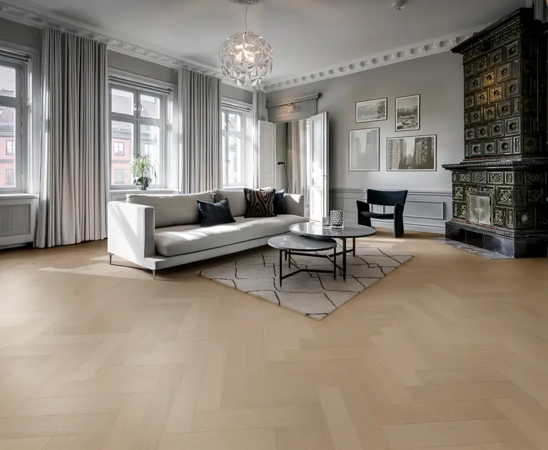 Spacious living room with a white sofa, round coffee table, patterned rug, large windows, and a decorative tiled stove.