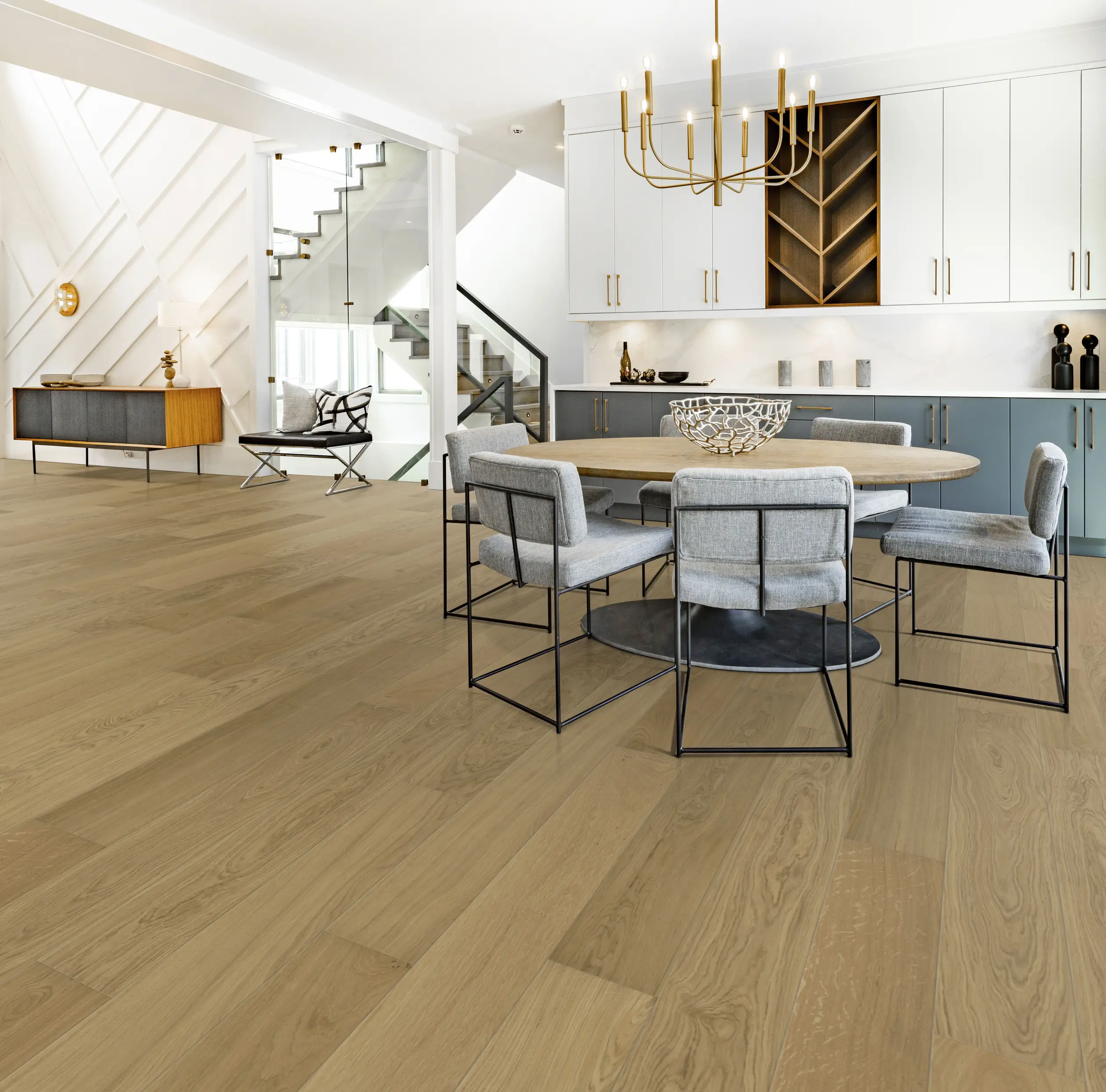 Modern open-plan kitchen and dining area with light wood flooring, round table with gray chairs, chandelier, and built-in shelves.