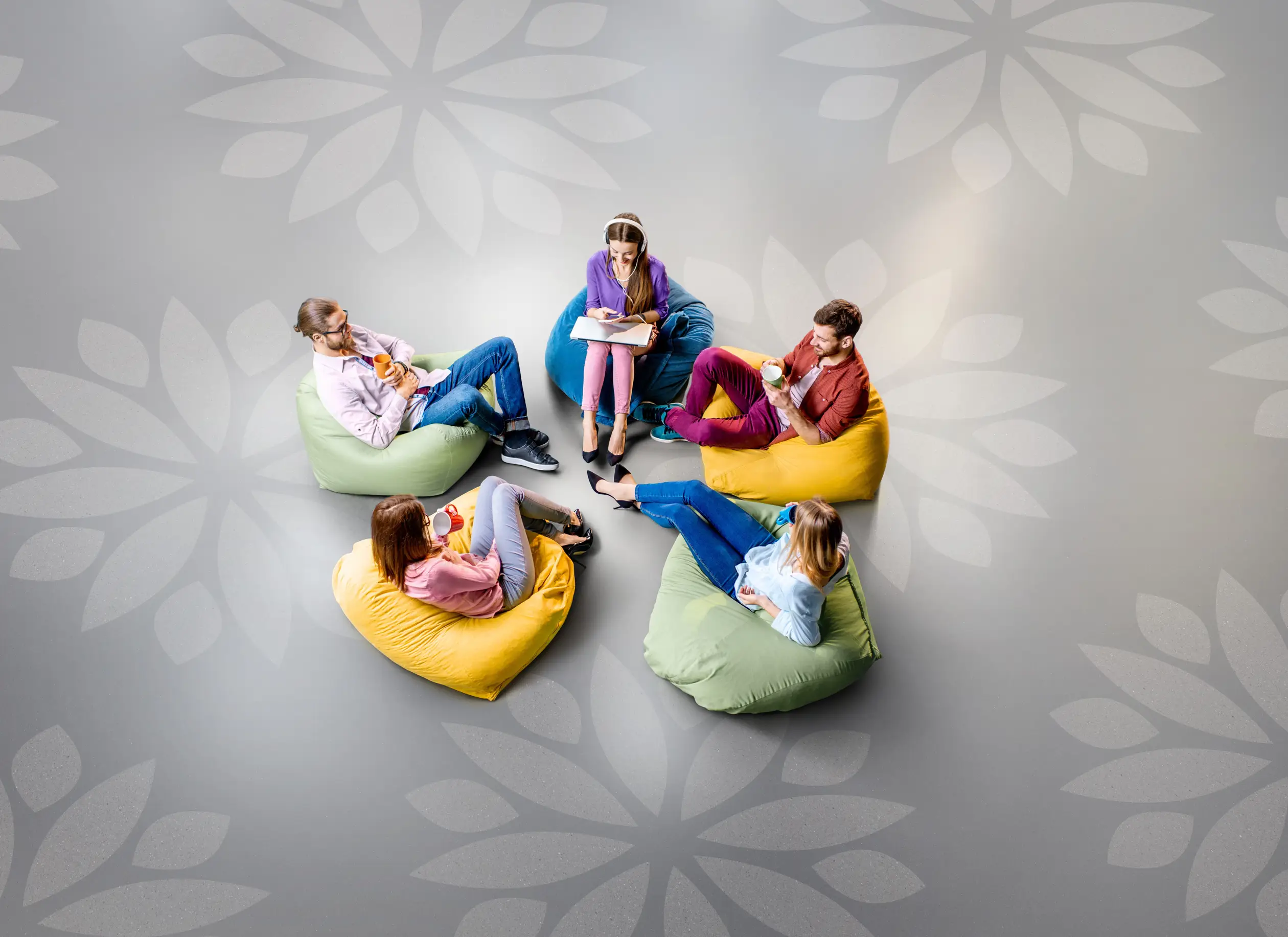 Five people sitting on colorful bean bags in a circle on a patterned floor, engaged in conversation.