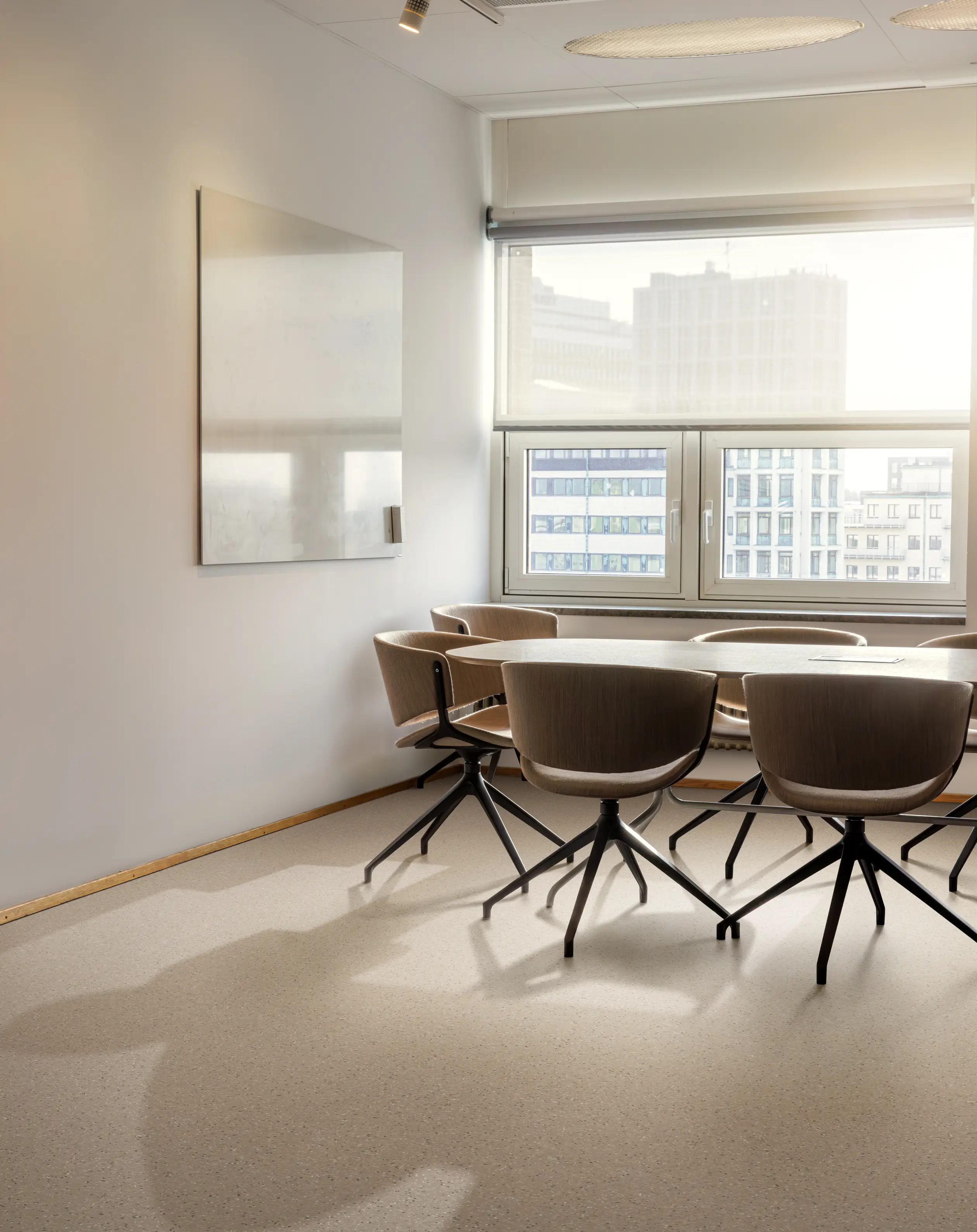 A modern conference room with a table, six chairs, a large window with city view, and a blank whiteboard on the wall.