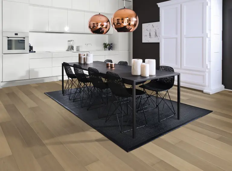 Modern kitchen with a long black dining table, black chairs, copper pendant lights, and white cabinetry. Light wood flooring and a dark accent wall.