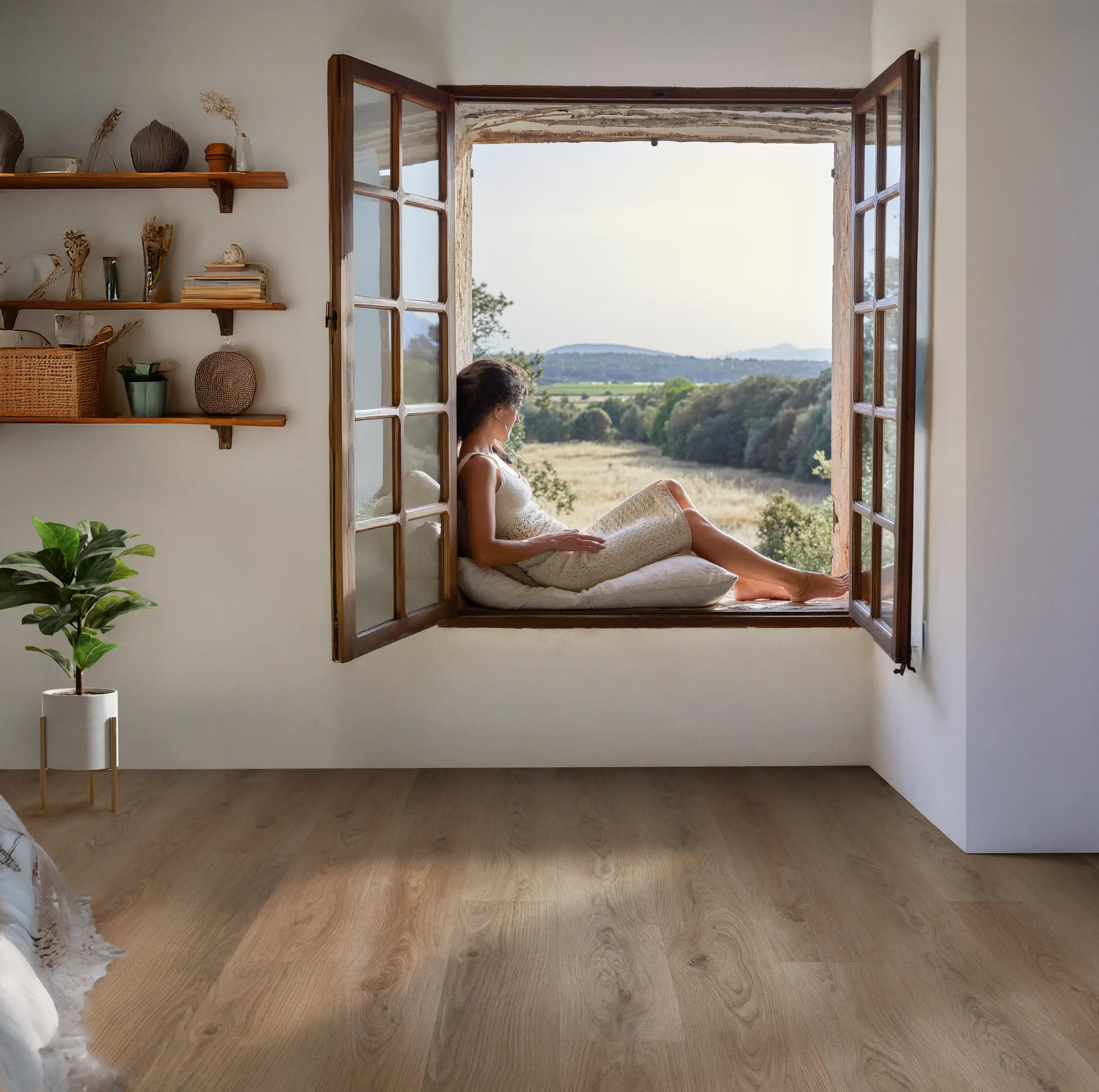 A person in a towel sits on a window ledge, gazing at the scenic landscape. Wooden shelves with decor, a plant, and wooden flooring in the room.