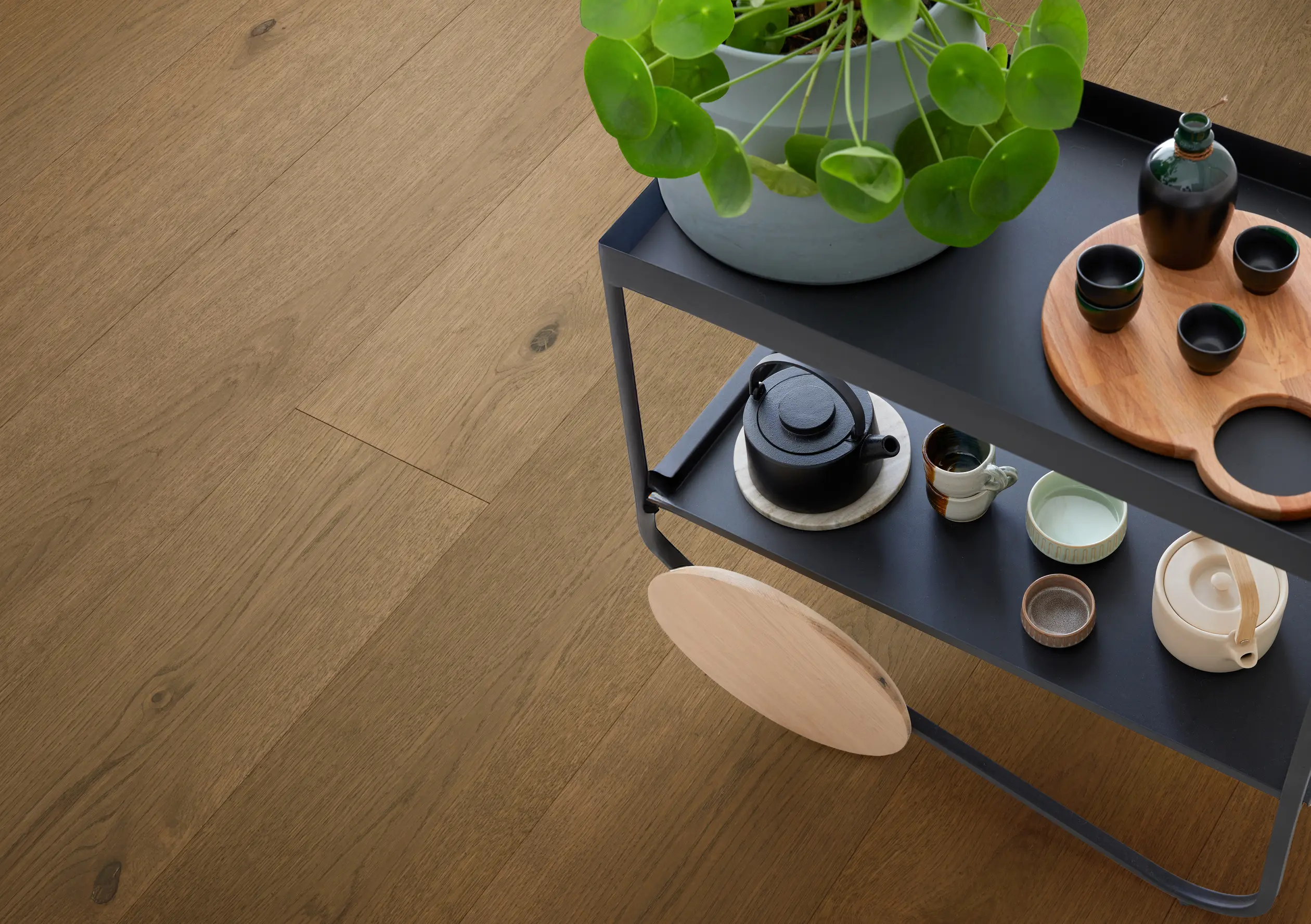 Top-down view of a black two-tier cart holding a potted plant and assorted teaware on an oak wood floor.