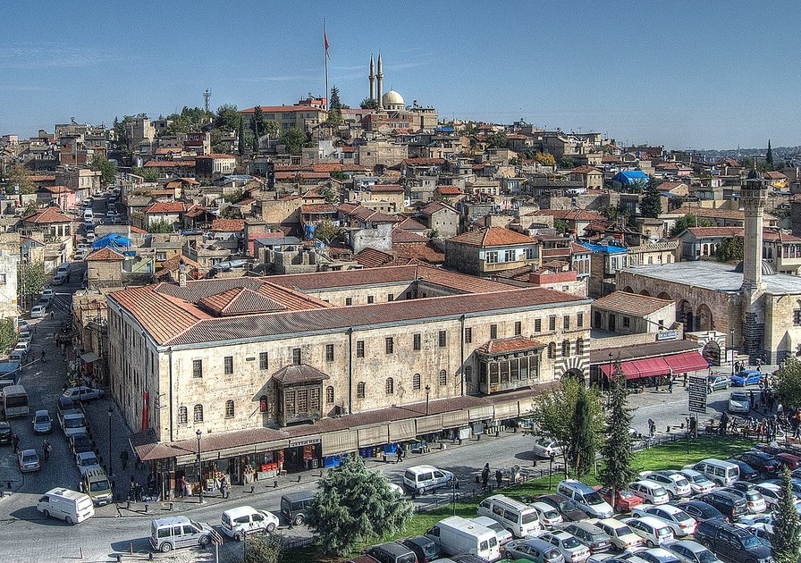A panoramic view of a historic city with densely packed buildings, a mosque, and bustling streets filled with cars and people.