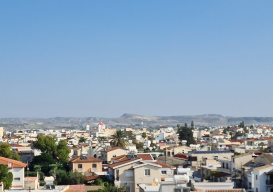 Panoramic view of a suburban landscape with numerous houses, greenery, and distant hills under a clear blue sky.