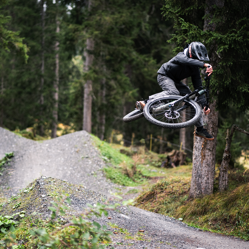 Fahrer der BIXS Traction Crew springt mit dem Mountainbike über einen Trail-Kicker im Wald