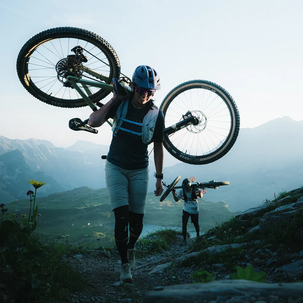 Mountainbiker trägt sein Bike auf der Schulter beim Aufstieg über einen Bergpfad