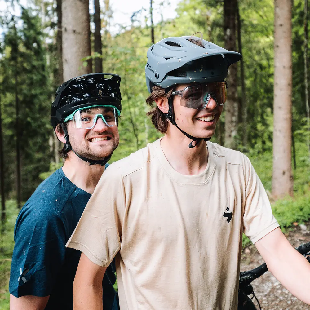 Zwei lachende Fahrer mit schlammbespritzten Gesichtern im Wald