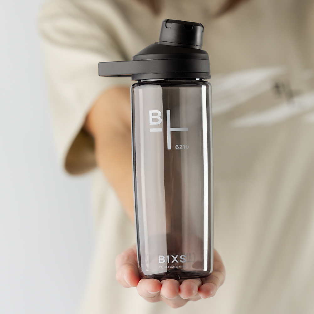 Eine Person, die eine durchsichtige Wasserflasche mit schwarzem Deckel in der Hand hält, auf deren Vorderseite das BIXS Logo zu sehen ist.