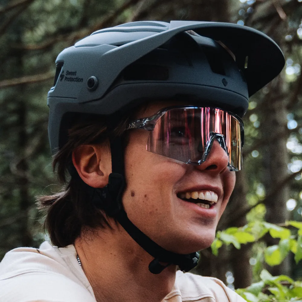 Lächelnder Fahrer mit Helm und verspiegelter Sportbrille im Wald