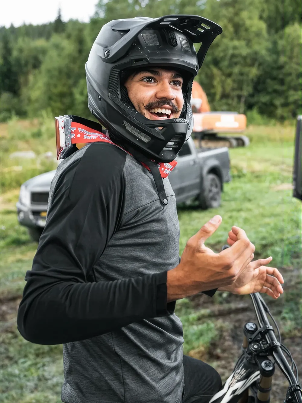 Vitor Buechli lacht mit Fullface-Helm neben seinem BIXS Bike, im Hintergrund Pickup und Baustellenfahrzeug
