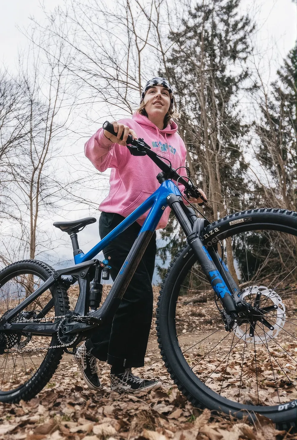 Michelle Neuner hält ihr blaues BIXS Dirt-Bike, trägt pinken Hoodie, herbstlicher Wald im Hintergrund